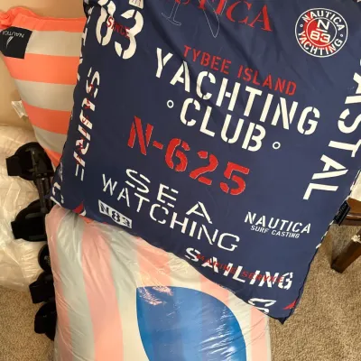 Nautica navy blue yachting club print throw pillow alongside coral striped bedding packaged in a Belk bag.