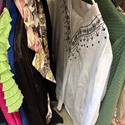 Selection of women's clothing hanging on a rack, featuring a white tunic top with black embroidered detailing.