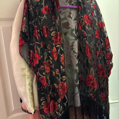 Black burnout velvet kimono featuring a red and gold floral pattern with black fringe hem, hanging on a door.