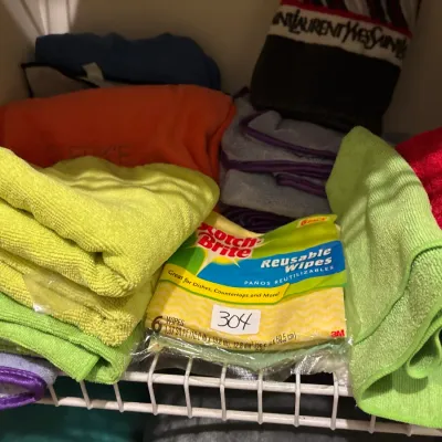 Assorted household cleaning supplies, featuring folded microfiber towels and an unopened pack of Scotch-Brite reusable wipes.