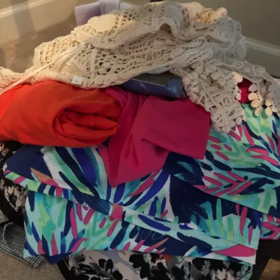 A folded stack of women's colorful clothing, including printed items, bright solid tops, and a crocheted lace garment on top.