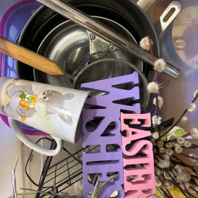 A collection of household goods and Easter decor, including nesting cake pans, a mesh strainer, squeegee, a bunny mug, and wooden...