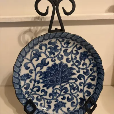 Blue and white porcelain decorative plate featuring intricate floral and scrollwork patterns with a scalloped edge, displayed on a black...