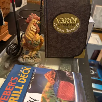 Collection of tabletop decor and books, including a small painted rooster figurine, a copy of Gunnars Treimanis' 'Vārdi',...