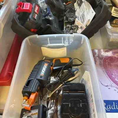 Collection of power tools and hardware accessories in plastic storage bins, including a Worx cordless screwdriver, charger, battery...