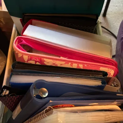 Collection of assorted office supplies including three-ring binders, spiral notebooks, and a pink floral pouch arranged in a tote.