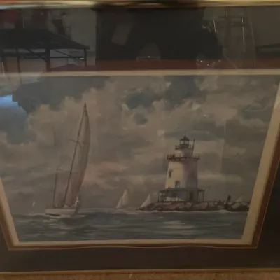 Framed nautical art print depicting a sailboat on choppy waters near a coastal lighthouse, presented under glass in a double mat and slim...