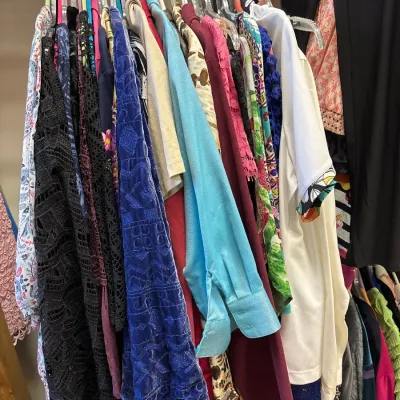 Clothing rack filled with women's colorful tops, blouses, and dresses in various fabrics and patterns.
