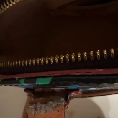 Interior and zipper detail of a patterned designer handbag, showing heavy wear and fraying along the leather tab.