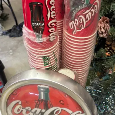 Vintage Coca-Cola wall clock with silver frame displayed alongside stacks of vintage Coca-Cola paper cups.