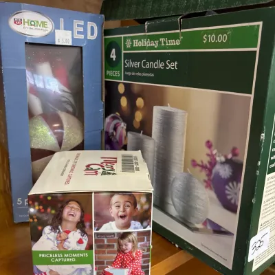 Selection of boxed Christmas decor items including a 4-piece Holiday Time silver candle set, an LED ornament set, and a Merry Cam ornament.