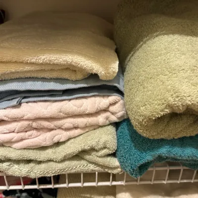 Stacks of folded bath towels and linens in various pastel and earth tone colors, neatly arranged on a closet wire shelf.