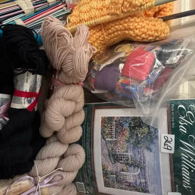 Crafting lot featuring yarn skeins, knitting needles, needlepoint floss, an in-progress knitted piece, and an Elsa Williams needlepoint...