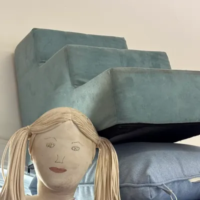 Handmade cloth doll with pigtails positioned in front of a blue foam pet staircase and stacked outdoor cushions.