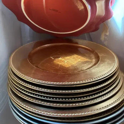 Stack of metallic gold beaded chargers alongside silver plates and a red fluted serving dish in a storage container.