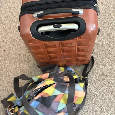 Copper-colored hardshell carry-on suitcase alongside a colorful geometric pattern fabric duffel bag.