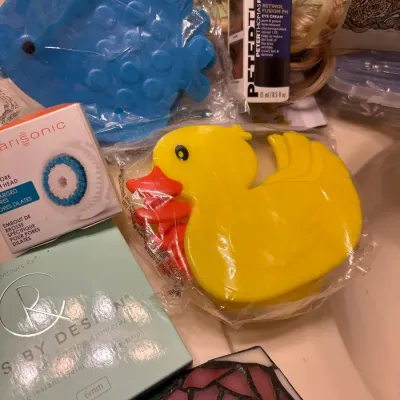 Collection of personal care products and novelties, including a Clarisonic replacement brush head, Peter Thomas Roth eye cream, and duck...