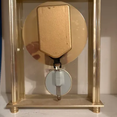 Back view of a vintage brass-tone glass mantle clock featuring a battery-operated movement labeled 'Taiwan' and a pendulum.