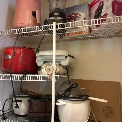 Collection of small kitchen appliances on wire shelving, including a pink air fryer, food processor, rice cookers, and a deep fryer.