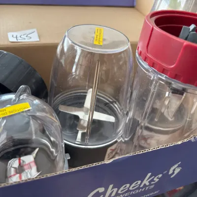 Collection of personal blender cups and blade attachments packed together in a cardboard box.