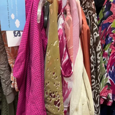 Clothing rack filled with women's patterned tops and dresses, featuring bold pinks, earth tones, and animal prints.