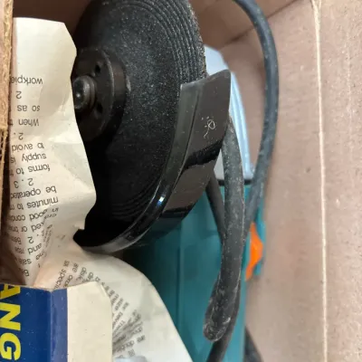 Corded electric angle grinder with attached grinding wheel and guard, stored in its original cardboard box with user instructions.