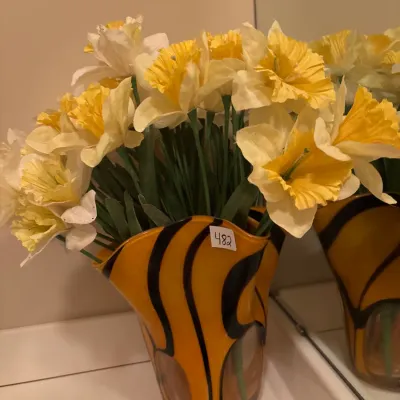 Wavy-edged yellow and black striped art glass vase filled with artificial yellow and white daffodils.