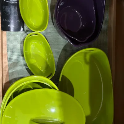 Collection of modern Curtis Stone ceramic cookware and bakeware, featuring vibrant lime green and eggplant purple pieces with integrated...