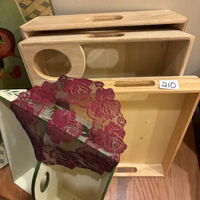 Set of unfinished light wood nesting trays with cutout handles alongside a floral lace textile piece and painted wooden caddy.