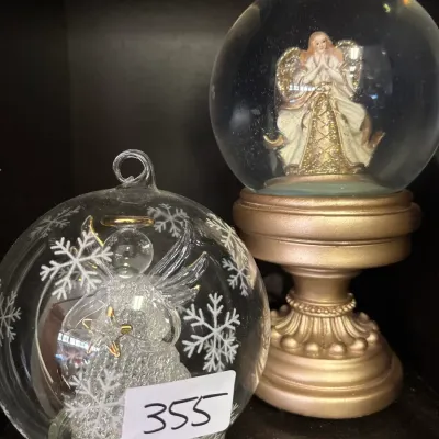 Two angel-themed Christmas decorations, including a clear glass ornament with a spun glass angel figurine and an angel snow globe on a...