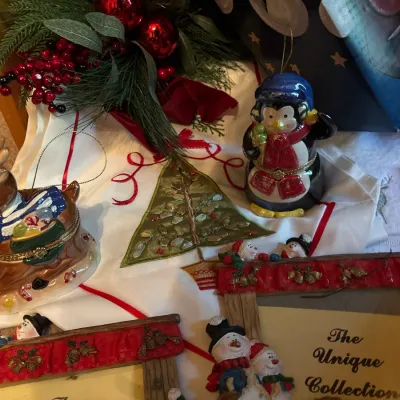 Collection of holiday decorations, featuring hinged ceramic trinket boxes shaped like a penguin and a reindeer, an embroidered table...