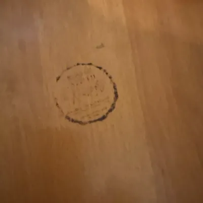 Faded manufacturer or maker stamp on a light-finished wooden furniture surface.