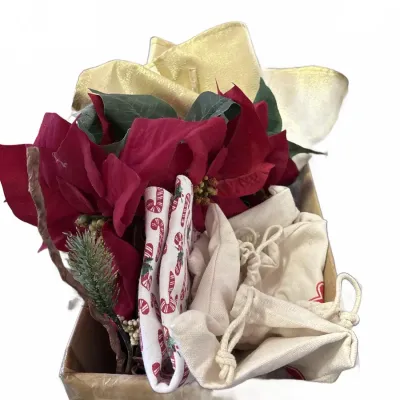 Box of holiday decor items including artificial poinsettias, a metallic gold ribbon bow, candy cane patterned fabric, and cloth...