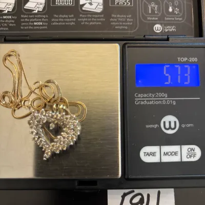 Gold chain with a diamond-encrusted open heart pendant shown on a digital pocket scale reading 5.73 grams.