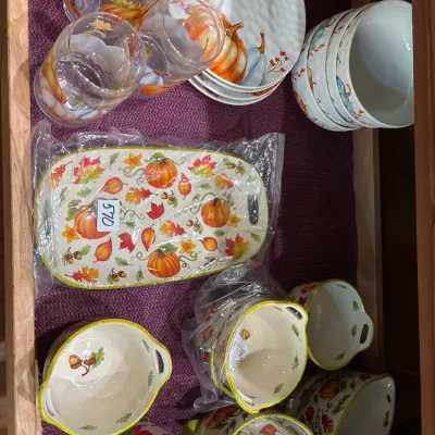 Collection of autumn and pumpkin-themed dishware, including glass stemless cups, ceramic plates, serving trays, and small bowls.