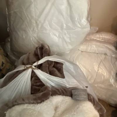 Collection of plush bedding items, including a brown fleece throw with sherpa lining and bagged queen-sized comforters or mattress pads.