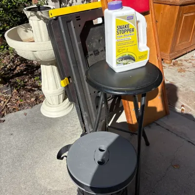 Collection of outdoor and household items including a bottle of Snake Stopper repellent, folding stools, a portable sawhorse, and an...