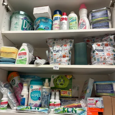 White storage cabinet filled with various household cleaning supplies, laundry detergents, stain removers, and moisture eliminators.
