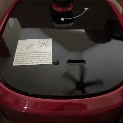 Red electric multi-cooker lid with safety instructions and chrome release valve handle.
