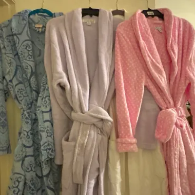 Trio of plush women's bathrobes hanging in a row, featuring a blue patterned fleece robe, a light purple plush robe, and a pink...