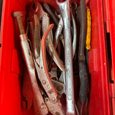 Red plastic tool box filled with assorted hand tools, including drop-forged wrenches and locking pliers showing light wear and surface rust.