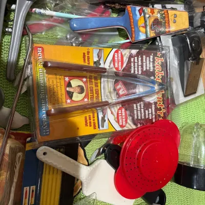 Assorted kitchen tools and gadgets, including a packaged Kake Kut'r cake server, a painted pie server, and various plastic utensils.
