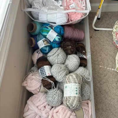 Large clear storage bin filled with various skeins and balls of knitting yarn, including plush chenille and marbled wool blends.