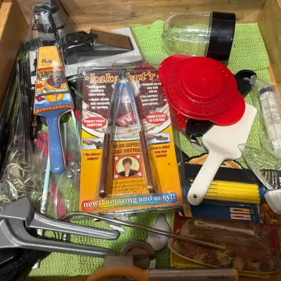 Kitchen drawer packed with assortment of novelty gadgets and utensils, including a vintage packaged Kake Kut'r, pie servers, and...