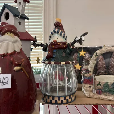 Collection of festive holiday decor items, including a ceramic Santa figurine, a snowman glass jar lantern, and a winter-themed...
