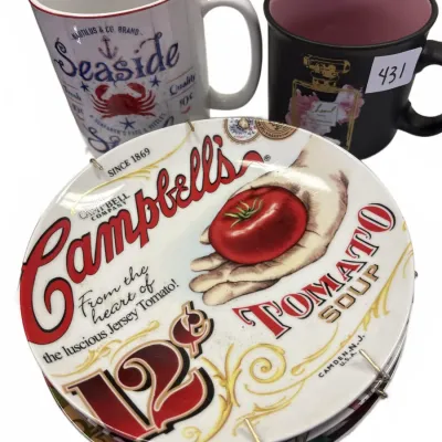 Set of collectible kitchenware including a Campbell's Soup decorative plate with display hanger, a nautical Seaside mug, and a black...