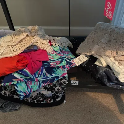 Piles of women's contemporary clothing, featuring colorful tropical print pieces, crochet tops, and items with original store tags...