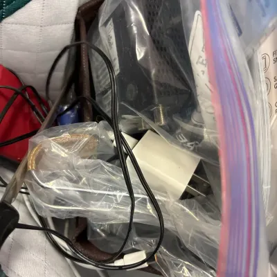 Assorted small electronics, power adapters, and cables stored in clear plastic bags inside a container.