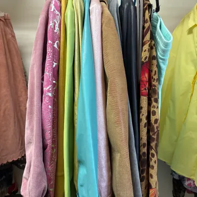Collection of colorful women's jackets and outerwear hanging on a closet rack, featuring suede, leather, metallic, and patterned...