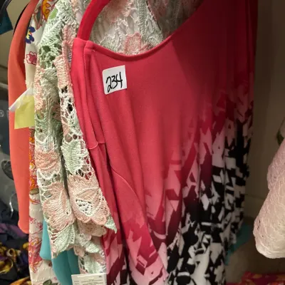 Selection of women's tops and blouses hanging on a rack, featuring a pink ombre patterned tunic and pastel lace garments.